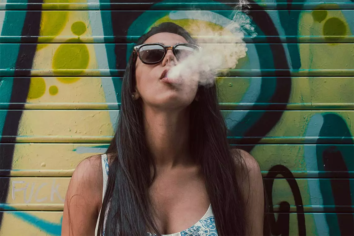 Woman smoking against graffiti wall.