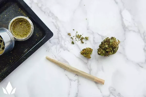 Cannabis nugs next to a joint, rolling tray, and grinder on a marble table.