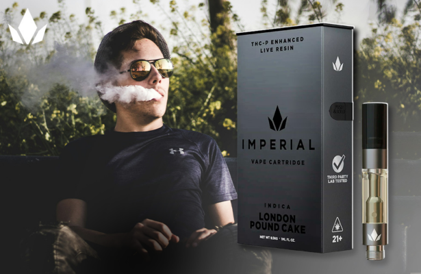 A man sits on a chair, exhaling smoke, with an Imperial vape cartridge of Indica London Pound Cake flavor beside him