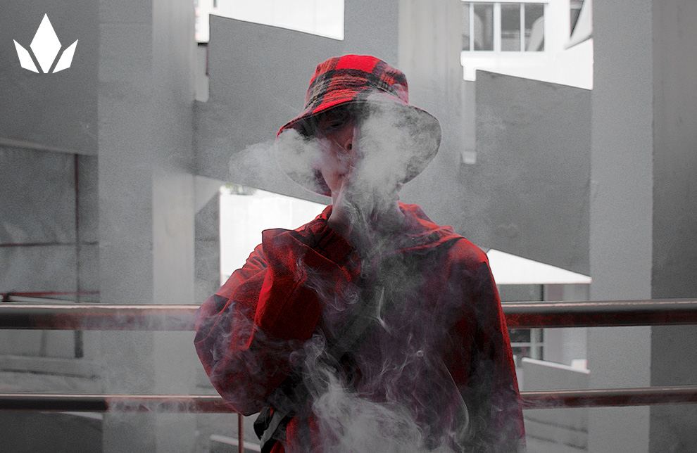 A man is standing in a white building and exhaling smoke