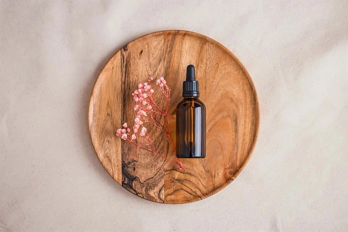 CBD Bottle on Wooden Tray Next to a Pink Flower