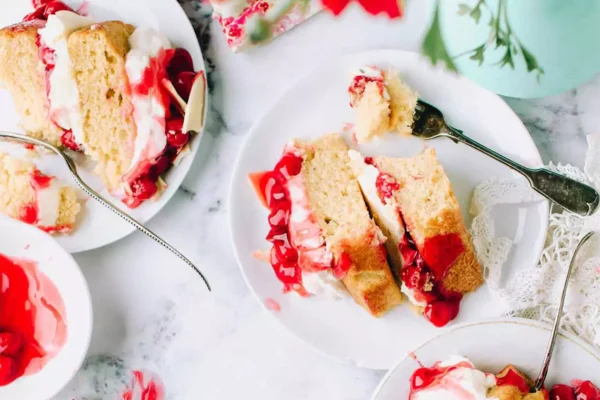 Multiple slices of strawberry and vanilla cake on plates with forks. 