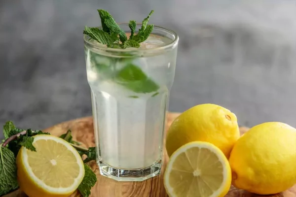 Cup of lemonade with mint leaves sitting on top of fresh lemons.